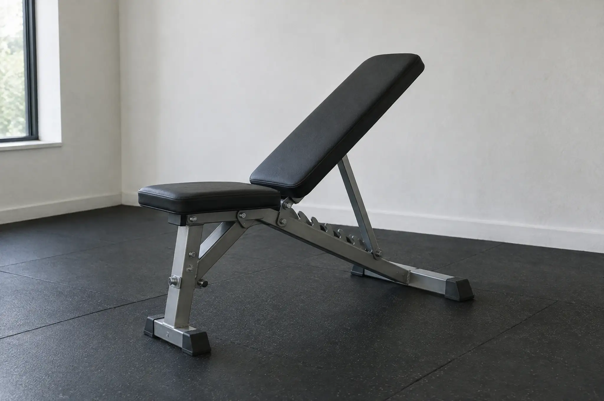 An adjustable weight bench on rubber flooring against a white wall